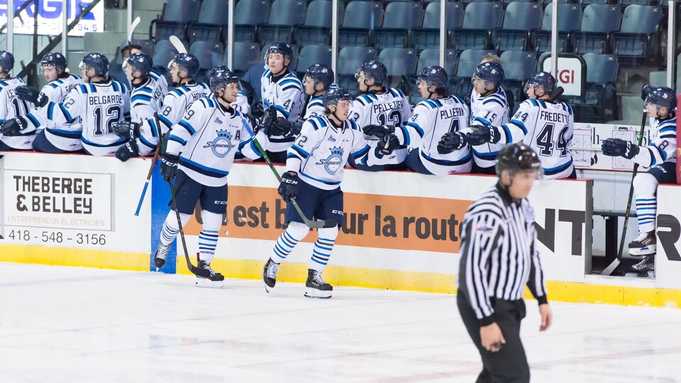 Deux joueurs de hockey reçoivent les félicitations de leurs coéquipiers devant le banc des joueurs.
