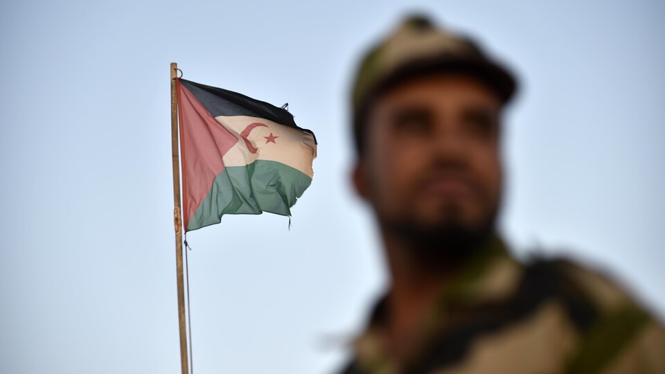 Un soldat en uniforme du Front Polisario pro-indépendance devant un drapeau sahraoui.