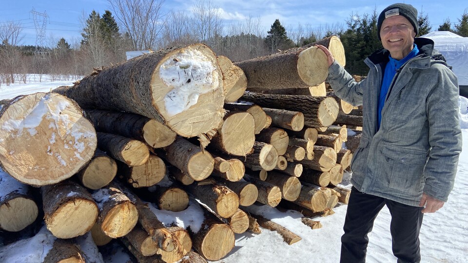 Denis Caouette posé devant des troncs d'arbres coupés sur son terrain en hiver.