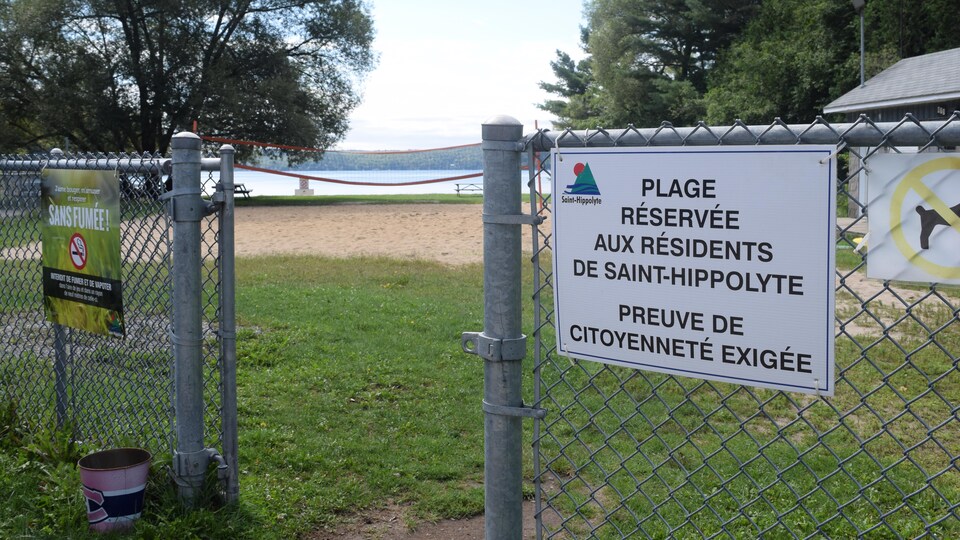 Une pancarte sur une clôture prévient que la plage, qu'on voit en arrière-plan, n'est accessible qu'aux résidents de Saint-Hippolyte