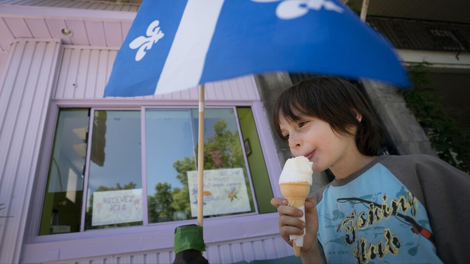 Un garçon mange une crème glacée près d'un drapeau du Québec.