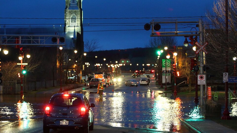 Une voiture circule sur une rue inondée au centre-ville de Sainte-Marie, en Beauce. La photographie a été prise de soir. 