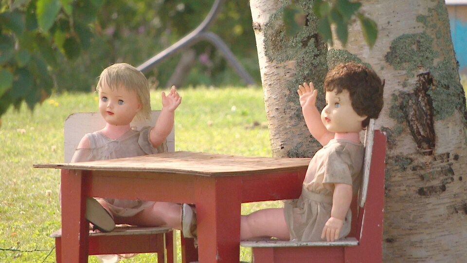 Deux poupées assises autour d'une petite table en guise de décorations sur la pelouse d'une résidence.