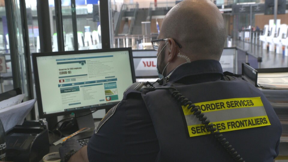 Un agent des services frontaliers travaillant à l'ordinateur, vu de dos.