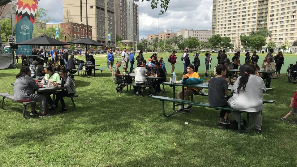 Des personnes assises sur des bancs installés autour des tables dans un jardin le 25 juin 2022 à Winnipeg.