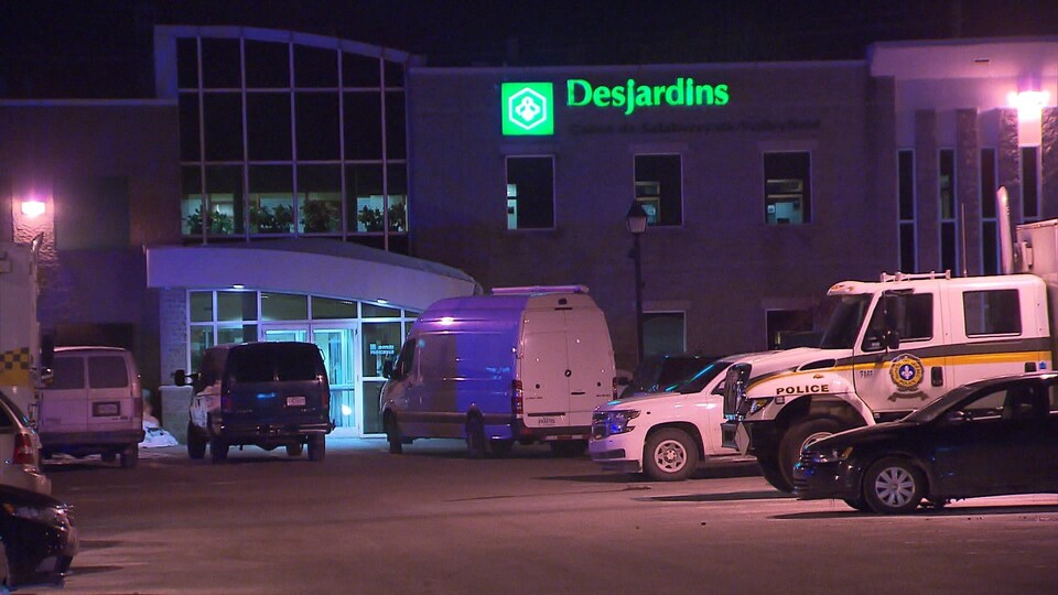 Dans le stationnement de la succursale de la Caisse Desjardins se trouvent des camions de la Sûreté du Québec.