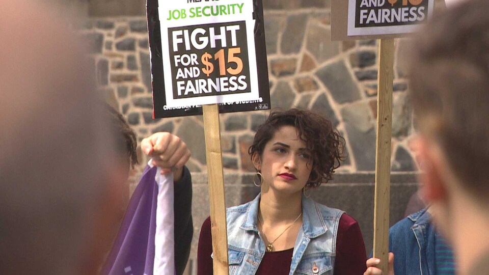 Manifestante tenant une affiche demandant un salaire minimum à 15 $ et de l'équité le 2 octobre 2018 à Halifax.