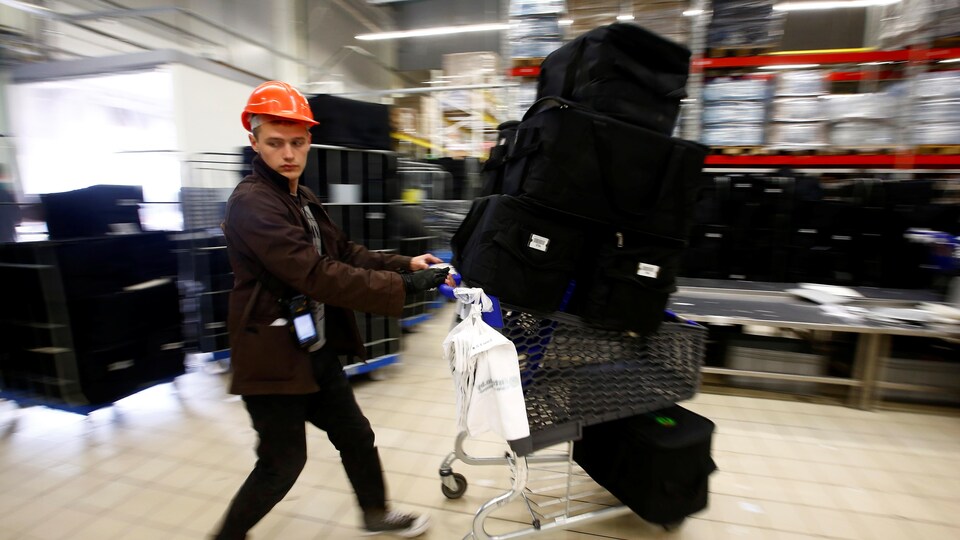 Un jeune homme coiffé d'un casque protecteur pousse un panier d'épicerie sur lequel des paniers de livraison sont empilés.