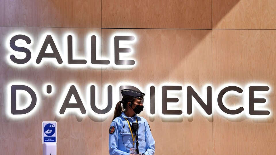 Une gendarme devant un signe indiquant « Salle d'audience ».