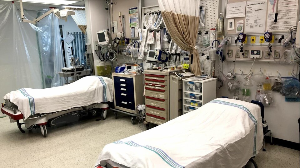 Deux lits entourés de matériel médical de soins intensifs dans une salle. 