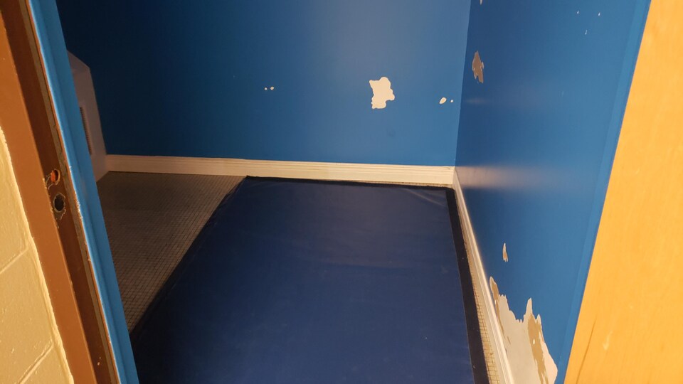 Une petite salle aux murs bleus avec un matelas recouvrant une partie du sol.