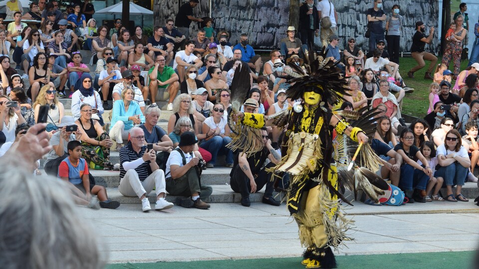Un homme en regalia danse devant un public, à l'extérieur.