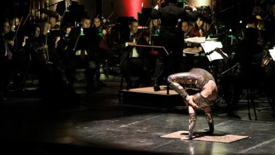 Une contorsionniste sur scène avec un orchestre symphonique. 