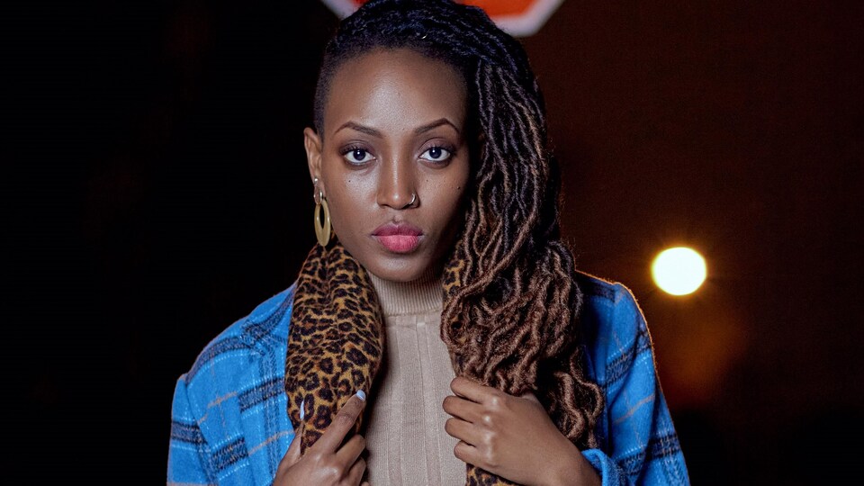Samantha Niyenimana dans la nuit, vêtue d'un manteau bleu et d'un foulard aux motifs léopard.