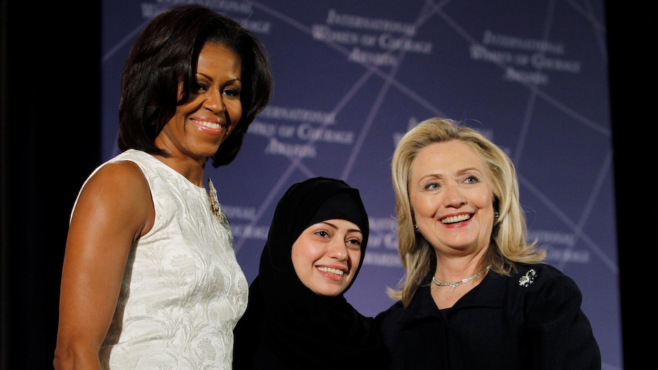 Trois femmes, dont l'une portant un hijab, sourient sur une scène.
