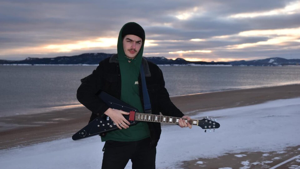Samuel Chiasson avec sa guitare au bord de l'eau en hiver.