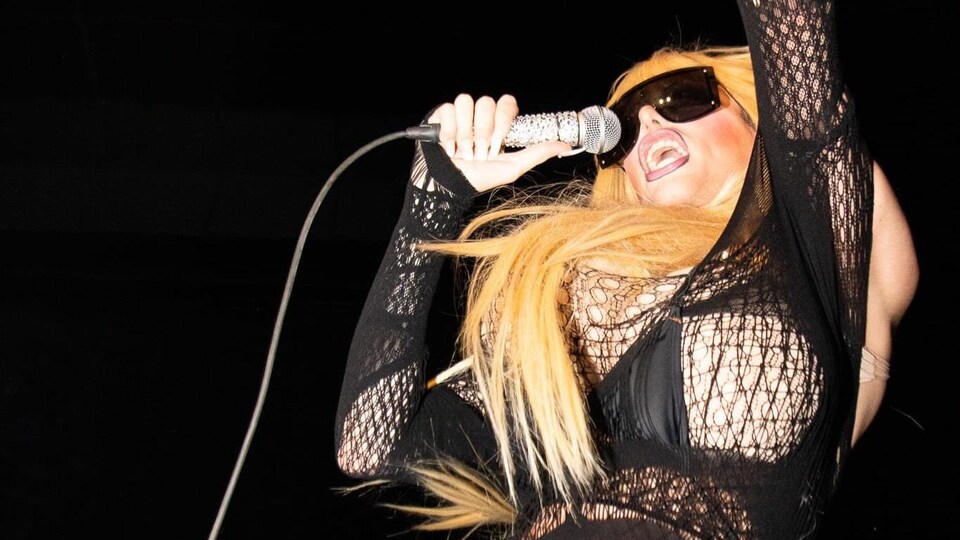 Une drag queen sur une scène avec un micro. 
