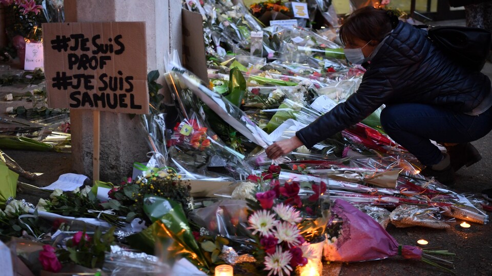 Une femme dépose une gerbe de fleurs au milieu de dizaines d'autres.