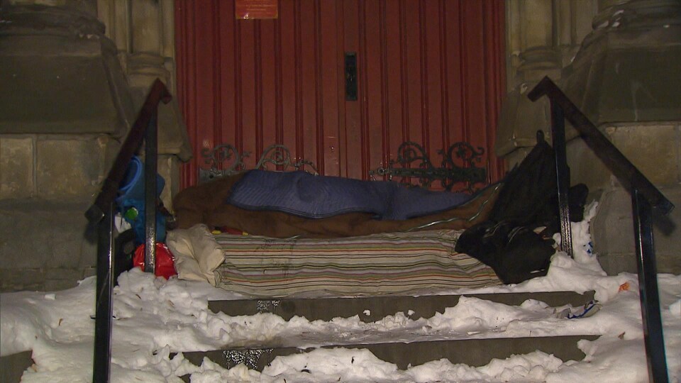 Couchette improvisée dans la neige, au haut d'un escalier, devant une porte