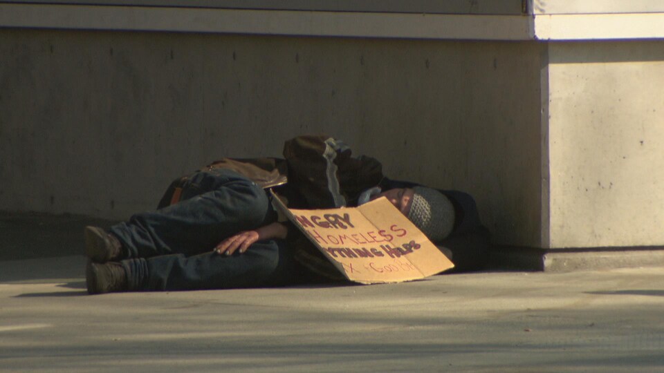 Un sans-abri est allongé sur le trottoir avec une pancarte en carton dans le Downtown Eastside, à Vancouver.