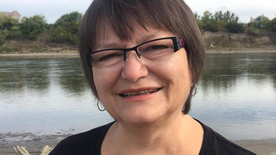 Une femme portant des lunettes et des créoles devant un plan d'eau.
