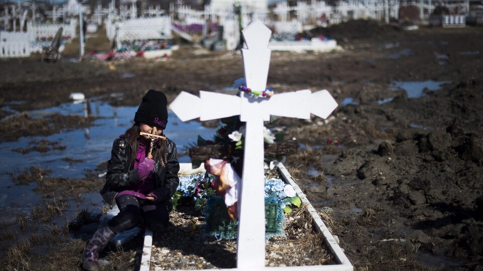 Une enfant se recueille à une tombe dans un cimetière dans la Première Nation d'Attawapiskat, en Ontario.