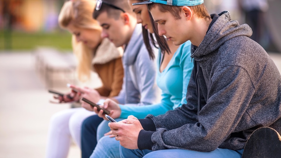 Un groupe d'adolescents assis à l'extérieur regardent leurs téléphones cellulaires.