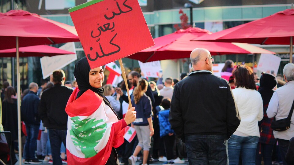 Une jeune femme entourée de manifestants tient une pancarte.