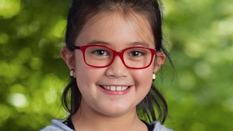 Une fillette portant des lunettes rouges qui sourit. 