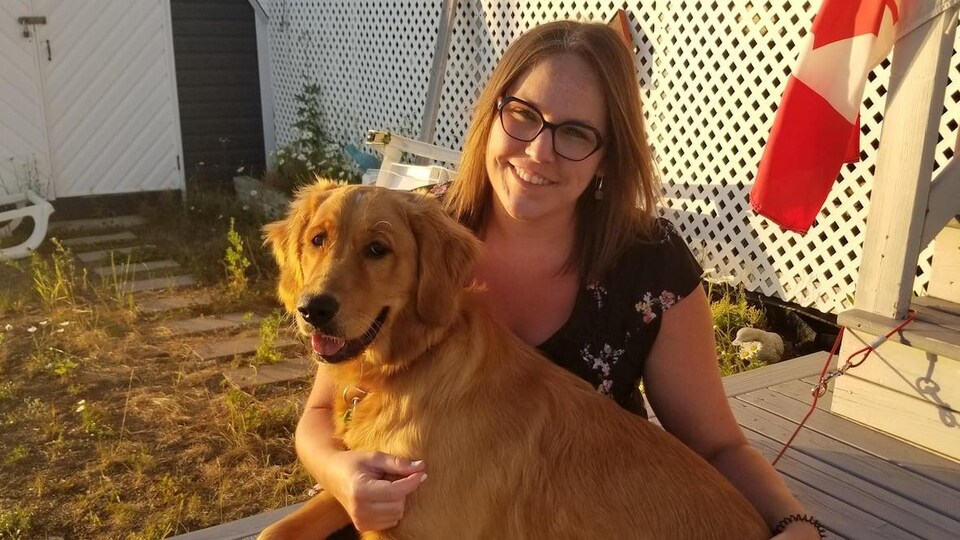 Sarah Sweet-Fortin, souriante, est assise dans un patio dans une cour avec un chien sur les genoux.
