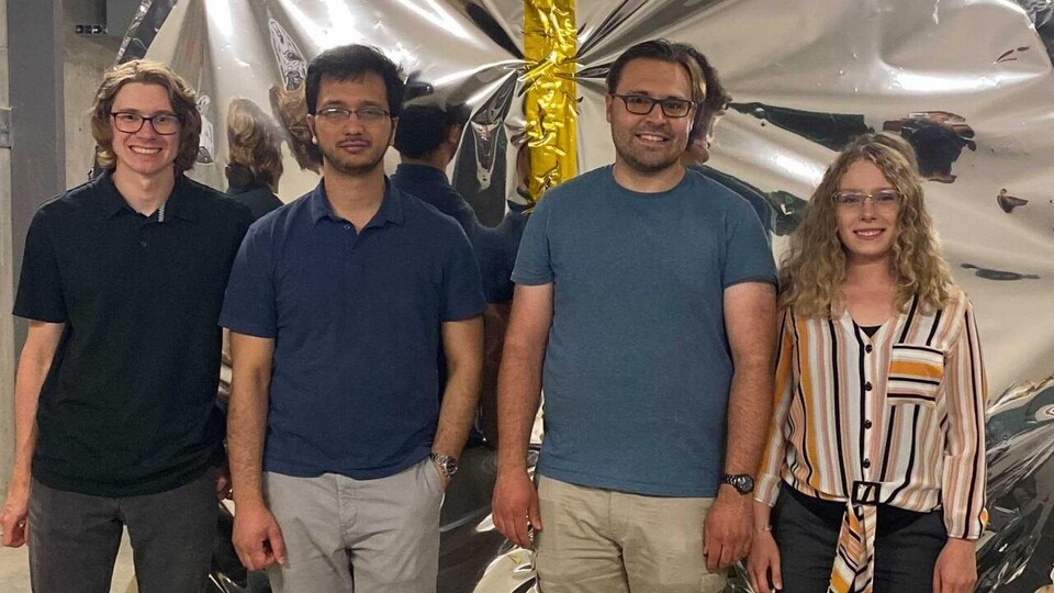 Quatre étudiants posent côte à côté devant une structure ronde en aluminium.