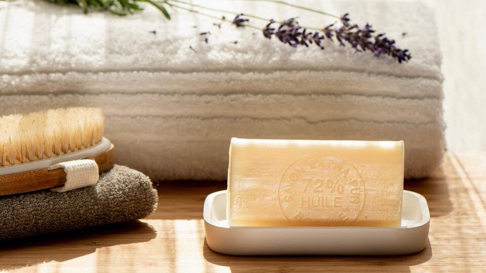 Un savon de Borale, manufacture de savon à Baie-Comeau, sur un savonnier avec brosse, brin de lavande et une serviette de bain.