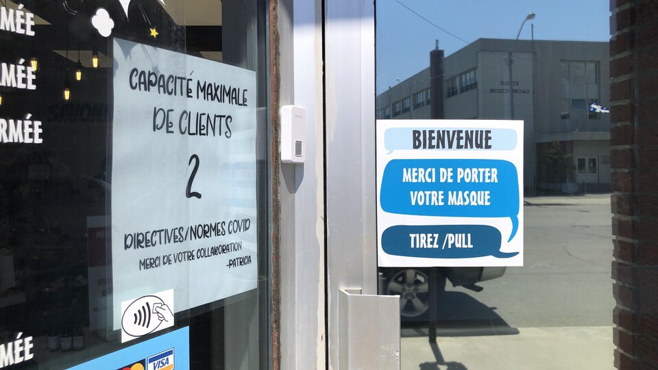Une affiche indique une capacité maximale de deux clients dans une vitrine de magasin.