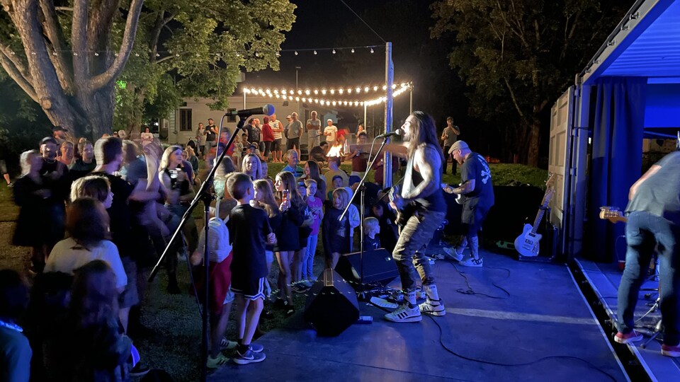 View from the side of the stage where we see a group including the singer facing the crowd in the evening.