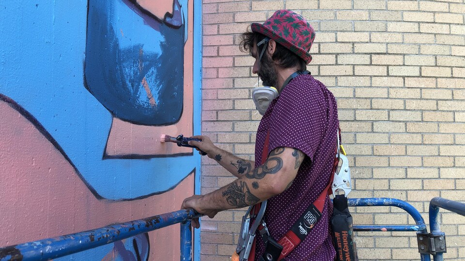 L'artiste visuel Sbuone en pleine action à Petit-Rocher. On l'aperçoit travailler à l'une de ses deux murales.