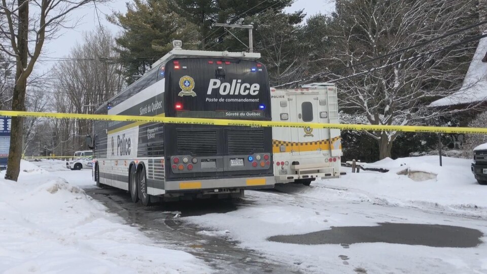 Des véhicules de police dans une rue résidentielle, en hiver.