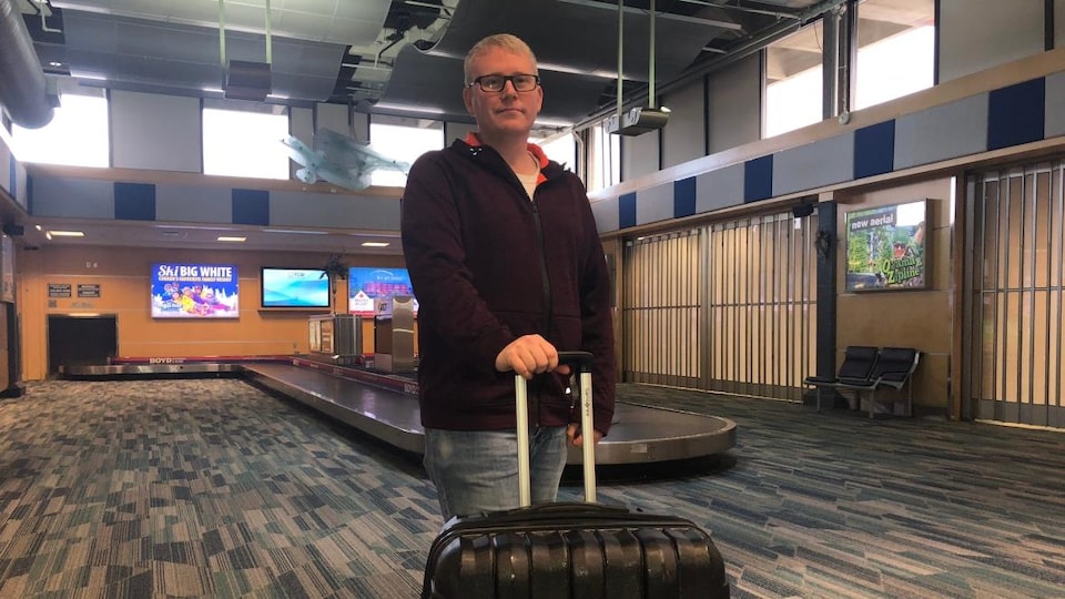 Un homme debout avec sa valise dans un aéroport.