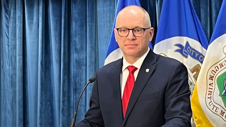 Le maire de Winnipeg Scott Gillingham en conférence de presse à l'hôtel de ville de Winnipeg, devant un rideau bleu et des drapeaux de Winnipeg, le 15 décembre 2022.