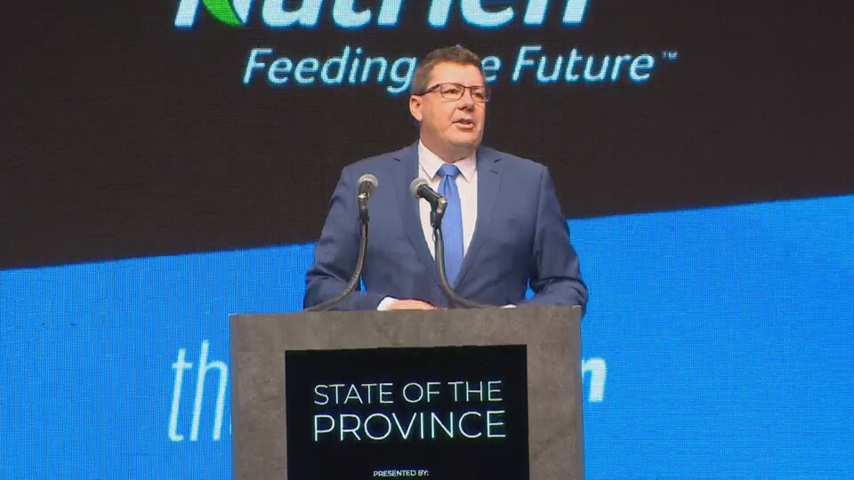 Le premier ministre de la Saskatchewan, Scott Moe, debout devant un podium à la chambre de commerce de Saskatoon.