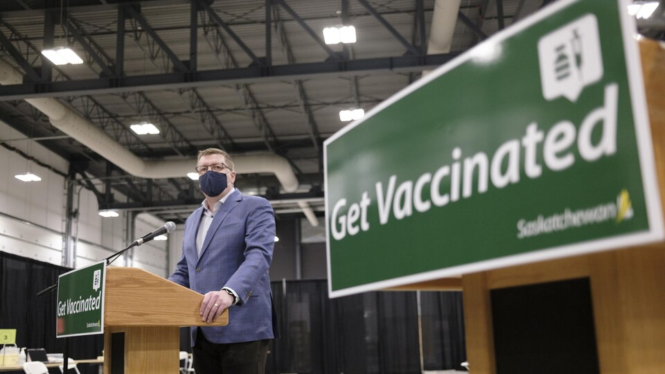 Scott Moe, devant un micro, près d'une pancarte sur laquelle est inscrit «Get Vaccinated».