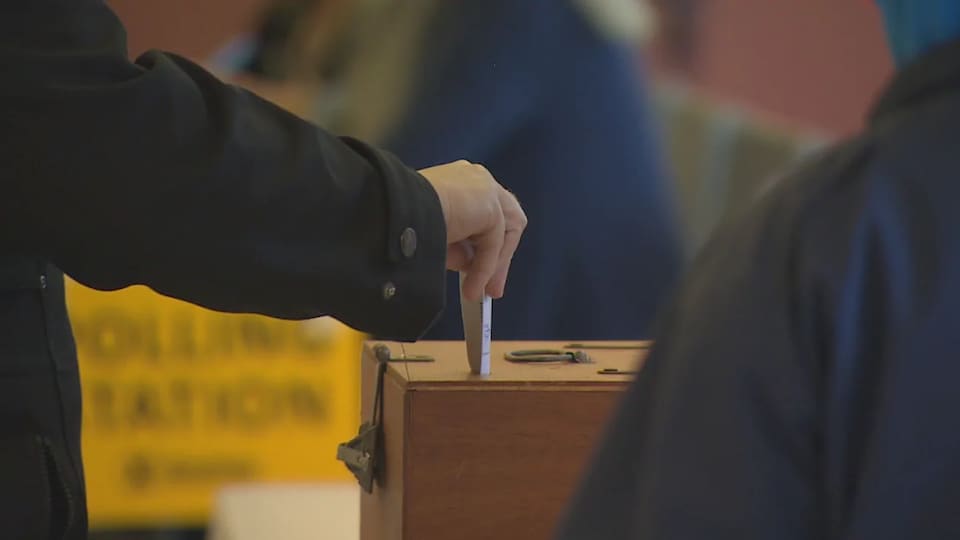 Un homme dépose un bulletin de vote dans une urne.