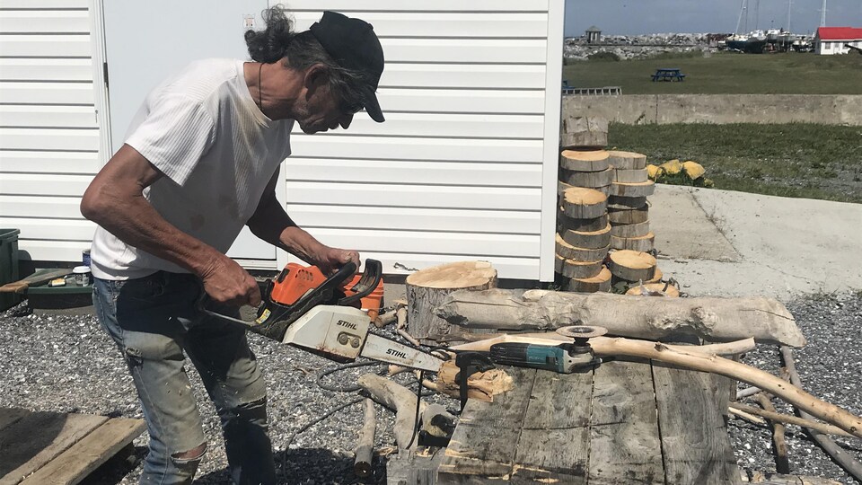 Un homme coupe un morceau de bois à l'aide d'une scie à chaînes.