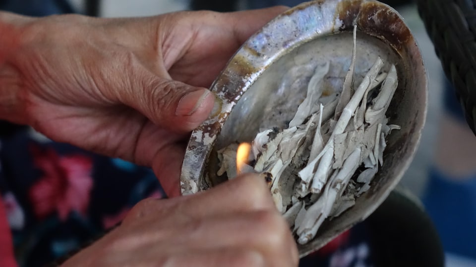 Une femme allume un briquet pour mettre le feu à un mélange de sauge posé dans un coquillage.