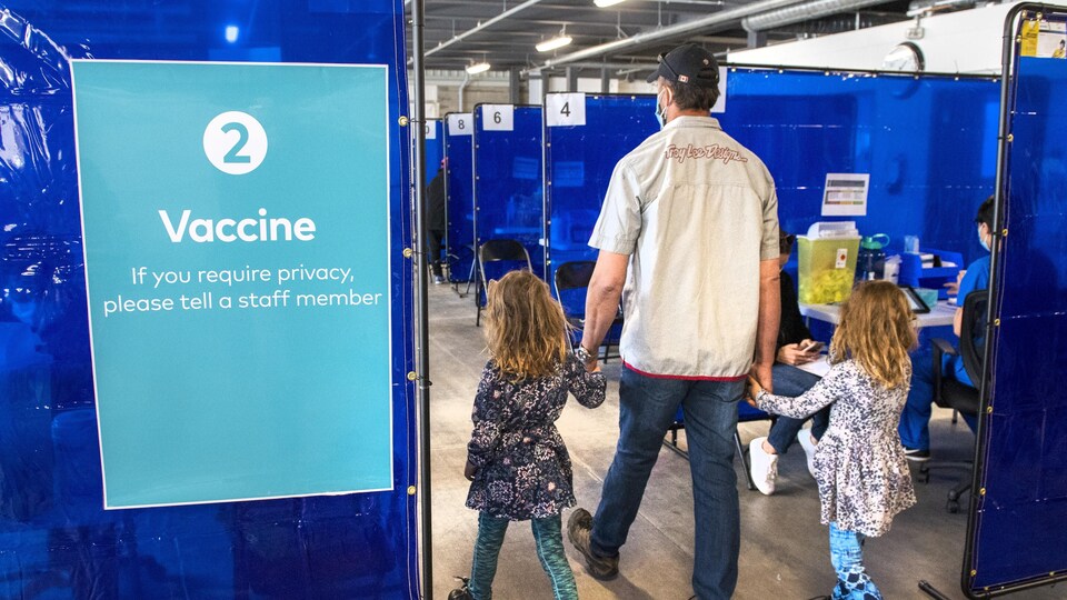 Un homme arrive dans un centre de vaccination avec deux fillettes.