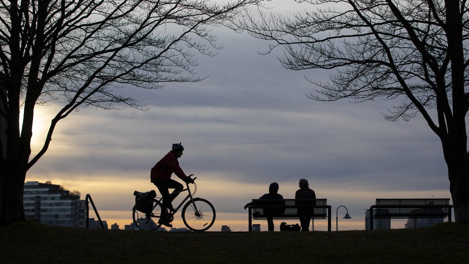 Un cycliste et des gens assis sur un banc de parc à Vancouver au coucher du soleil. 