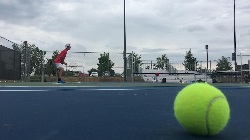 Un joueur de tennis attend un service, une balle à l'avant-plan.