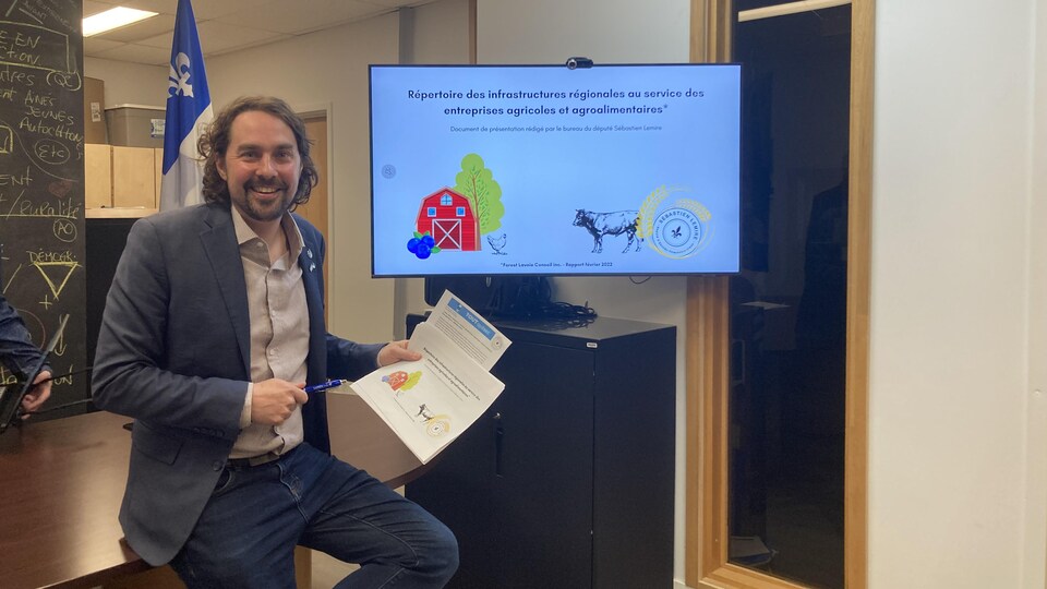 Sébastien Lemire, souriant, tient des documents dans ses mains.