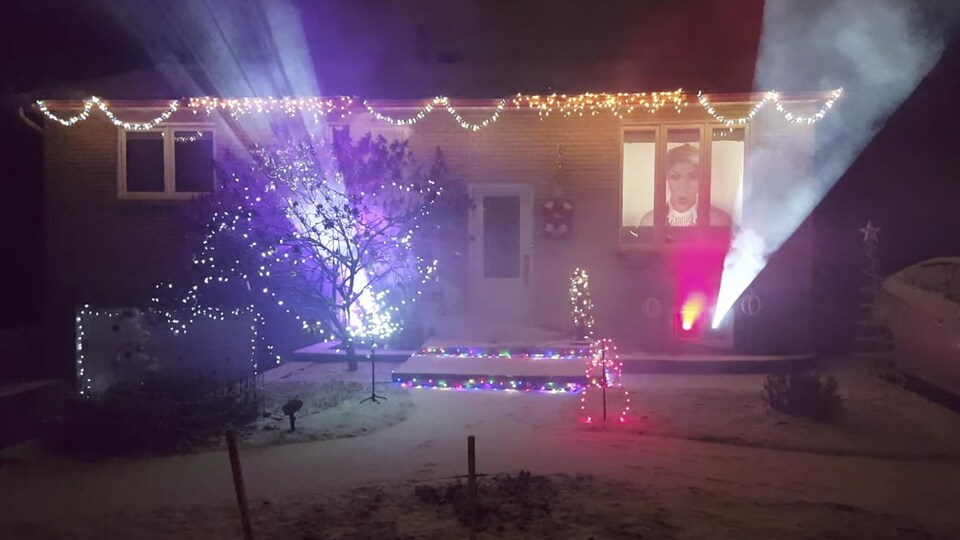 Des faisceaux de lumière sont projetés depuis l'intérieur d'une maison décorée pour les Fêtes.