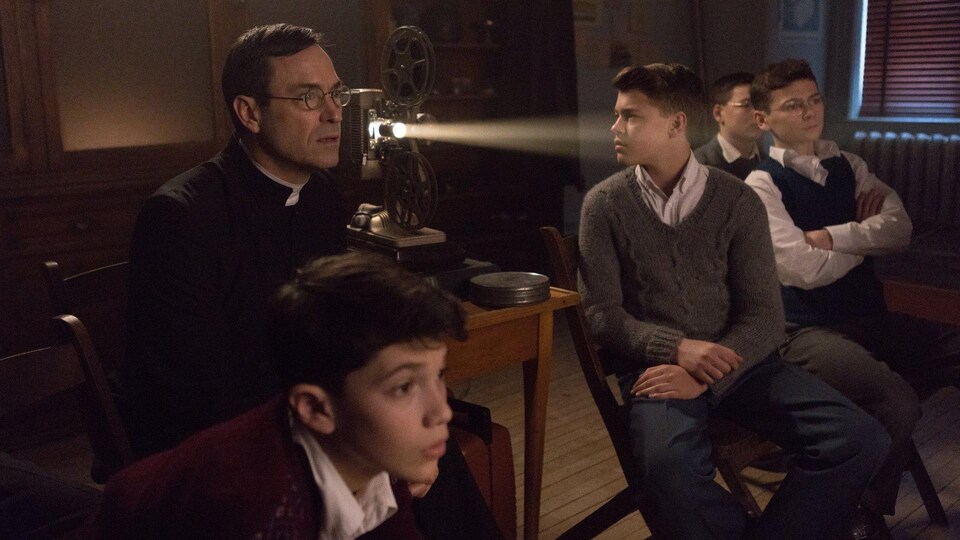 Un homme et quatre jeunes garçons regardent une projection de film dans une classe.