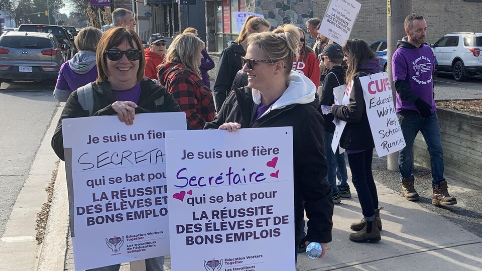 Deux grévistes tiennent des pancartes disant qu'elles sont des secrétaires.